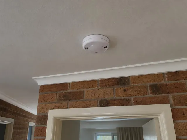 Ceiling-mounted smoke alarm above a brick interior wall and doorway in Swansea